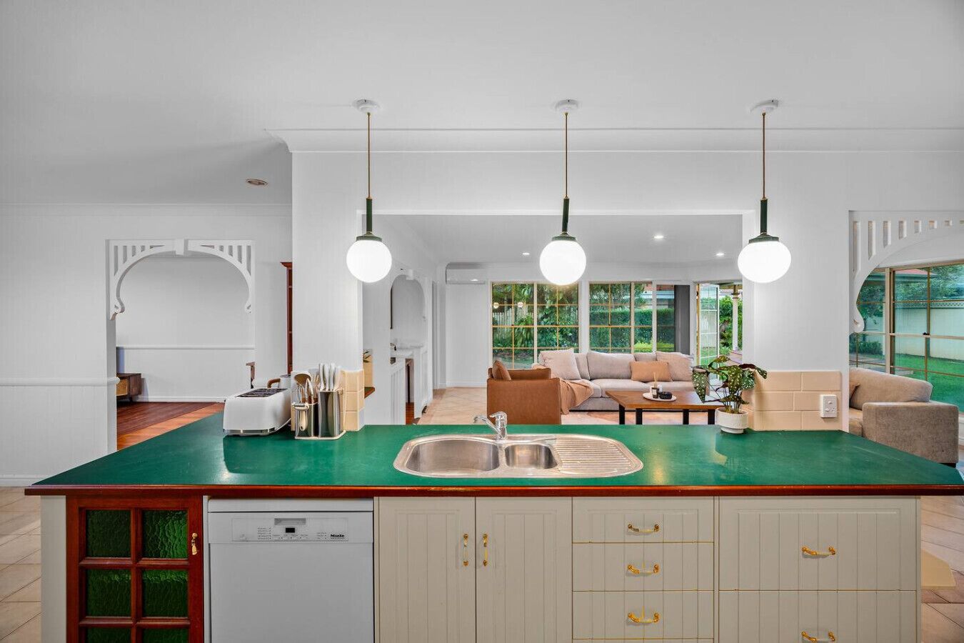 A modern kitchen with a green countertop, a built-in dishwasher, and a sink. There is a dining area with a sofa and a coffee table.