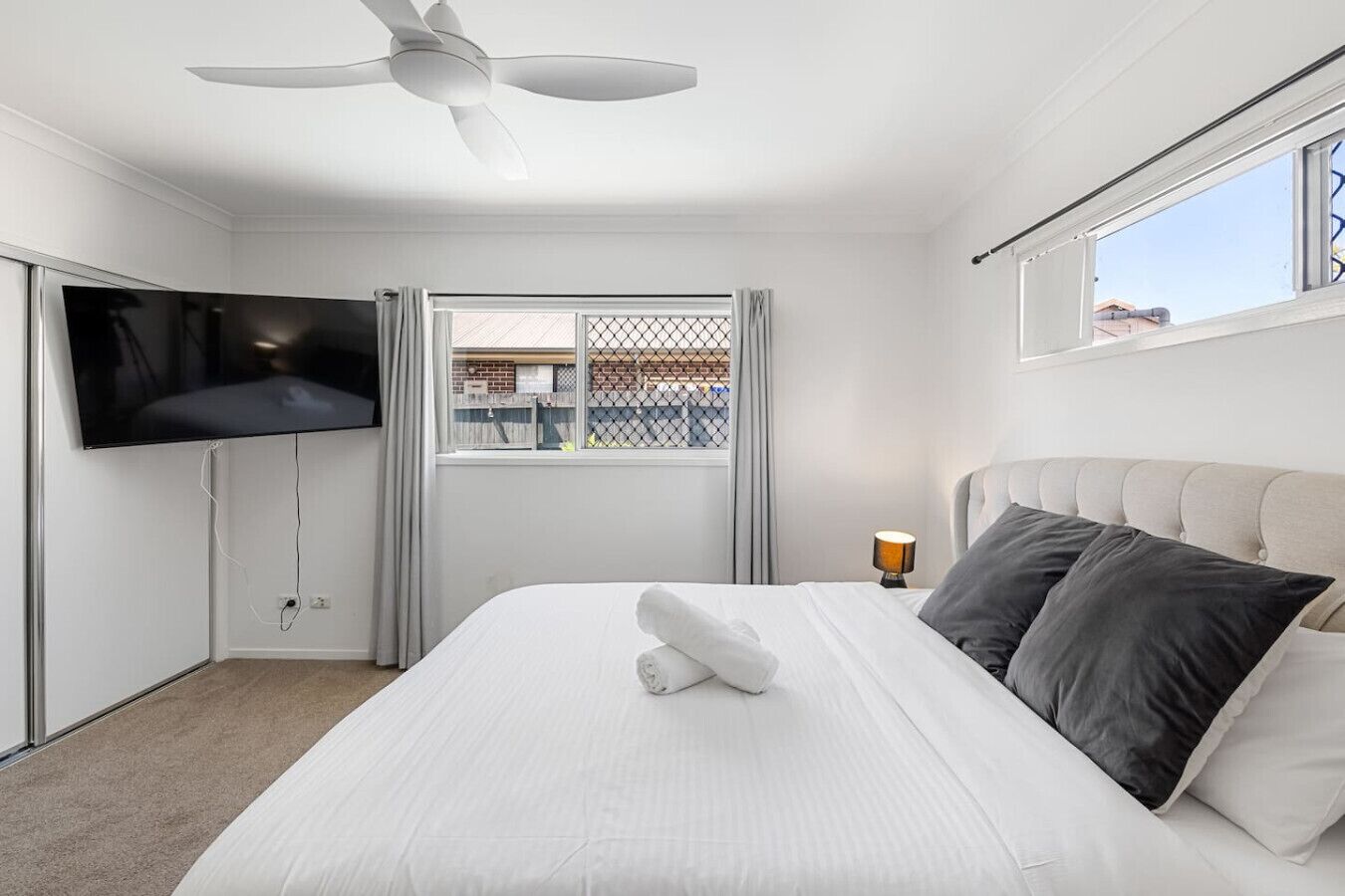 A hotel room with a bed, a ceiling fan, a TV, a window with a view, and a lamp.