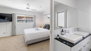 Ein modernes Schlafzimmer mit Bett, einem großen Spiegel, einem Fernseher und einem Badezimmer mit zwei Waschbecken.