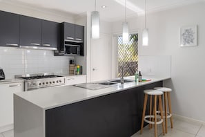 Une cuisine moderne dotée d’un îlot central, d’appareils électroménagers en acier inoxydable et d’un plan de travail noir.