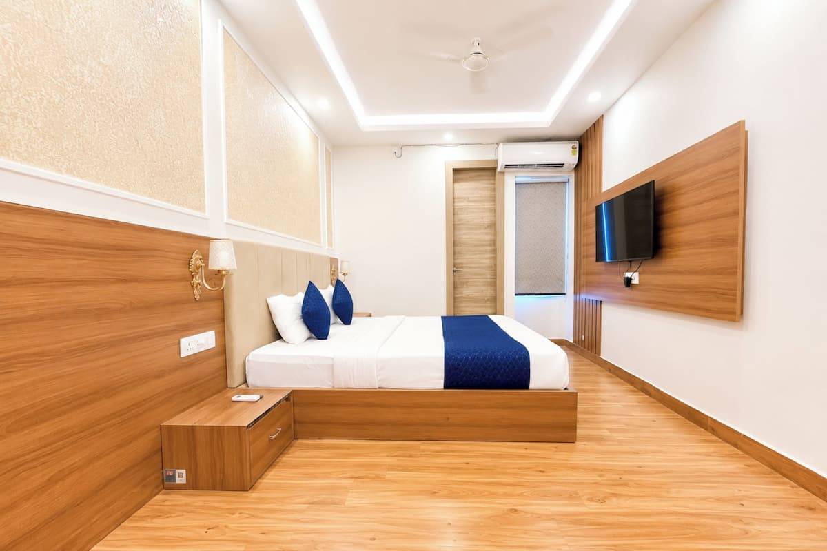 Ein modernes Hotelzimmer mit Holzboden, einem Bett mit weißblauer Bettwäsche, einem an der Wand montierten Fernseher und einem Deckenventilator.