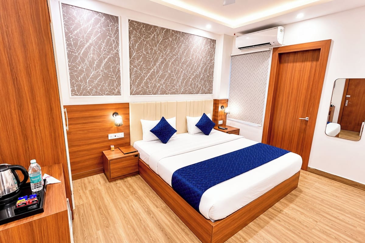 Ein Hotelzimmer mit einem Holzkopfteil, einem großen Bett mit blauer Bettwäsche, einem Nachttisch mit Lampe und einem Kleiderschrank.