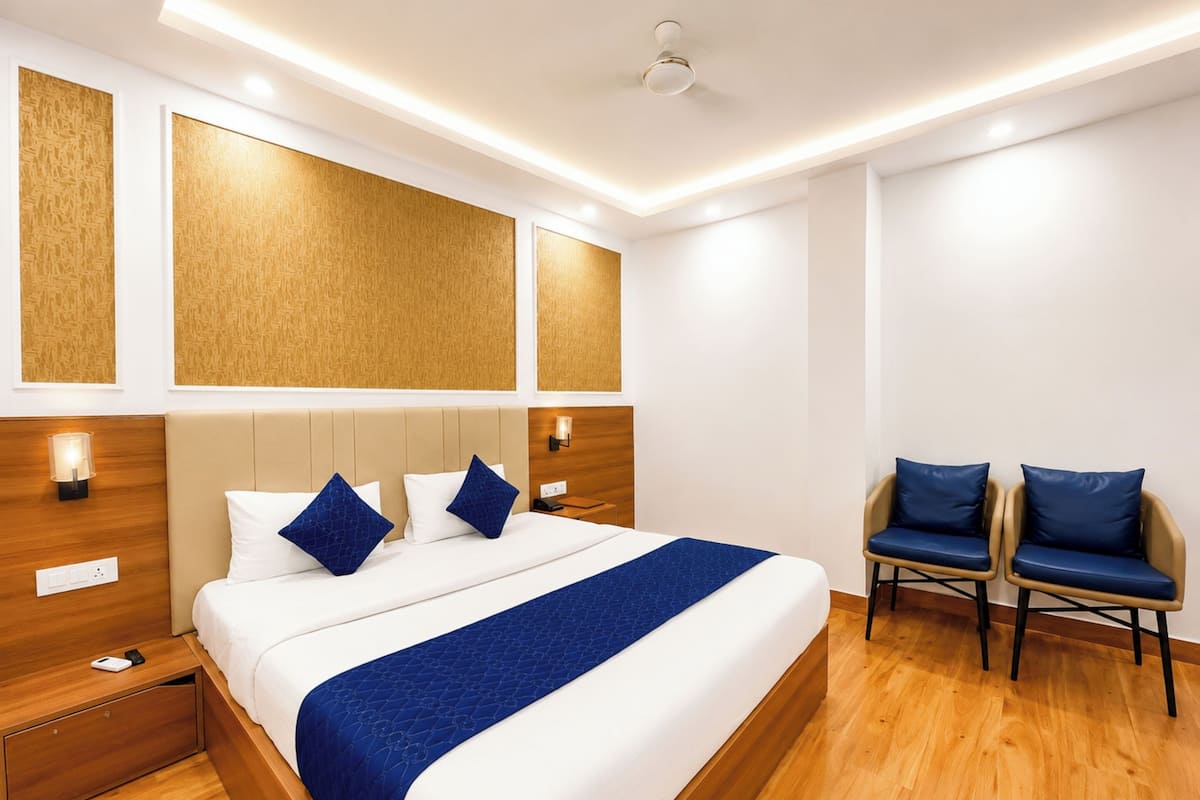 Ein Hotelzimmer mit einem großen Bett, einem Nachttisch, einem Schreibtisch, zwei Stühlen und einer Deckenleuchte.