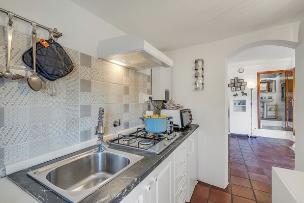 Una cucina moderna con lavello in acciaio inossidabile, piano cottura a gas e una pentola blu sul bancone.