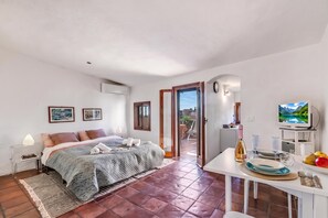 A bedroom with a bed, bedside tables, a TV, and a dining area with a table set for two. - Piccola Pigna - Terrazza Vista Mare Sanremo Studio, Sanremo, Italy (Sanremo)