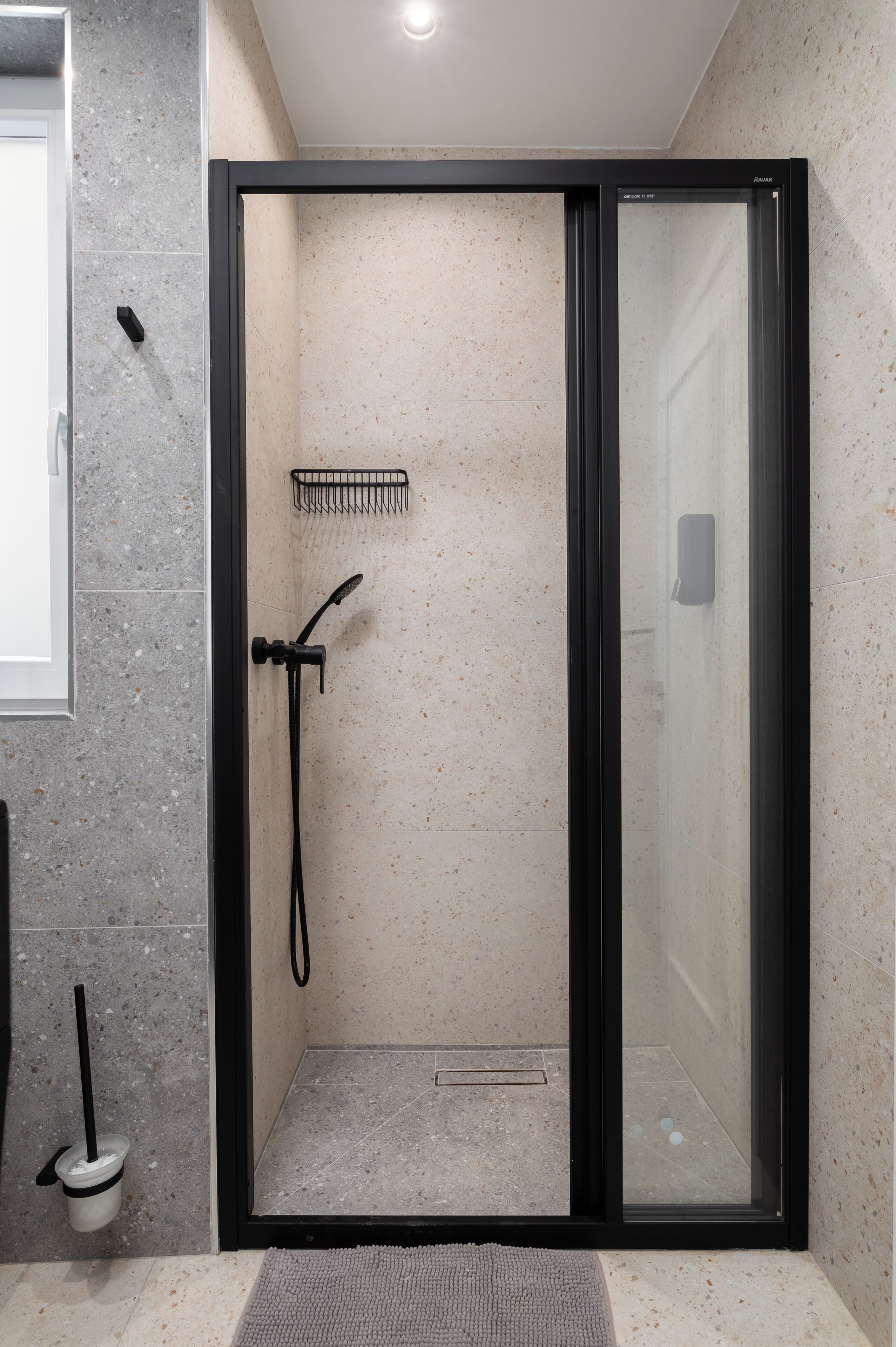 Un baño moderno con ducha de vidrio, cabezal de ducha manual y toallero.