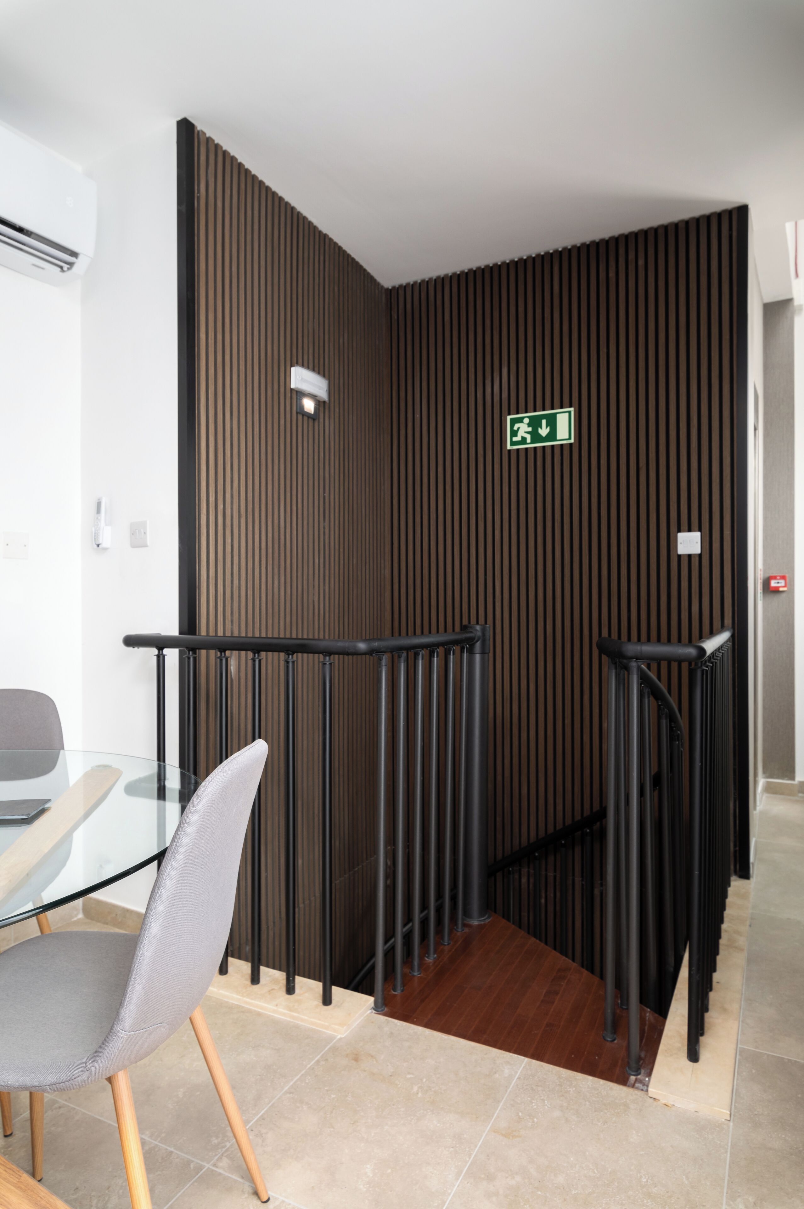 A modern interior with a glass table and chairs, a wooden slatted wall, and a black railing.