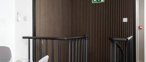 A modern interior with a glass table and chairs, a wooden slatted wall, and a black railing.