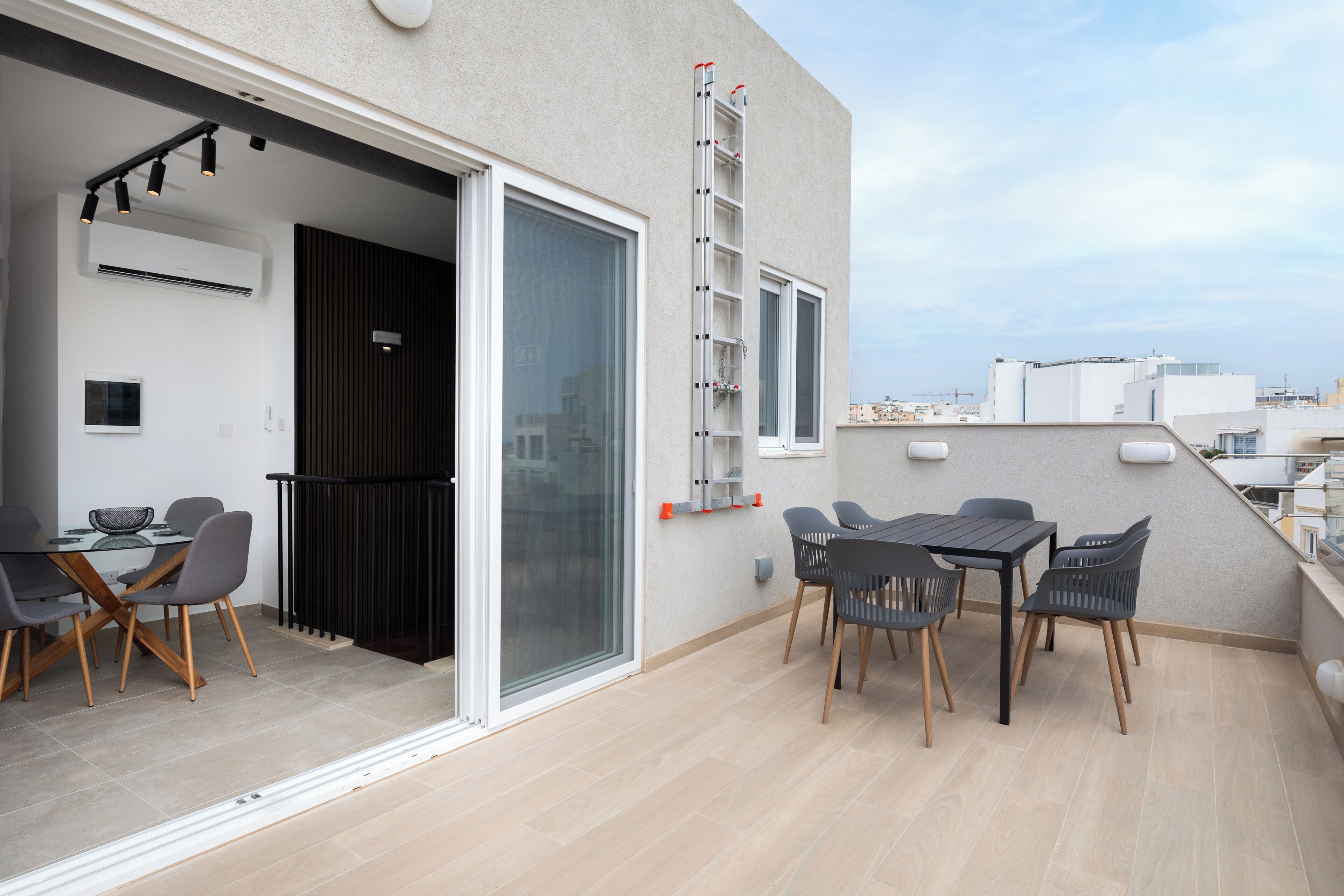 Une terrasse extérieure moderne comprenant un espace repas, une porte-fenêtre coulissante et un escalier en métal.