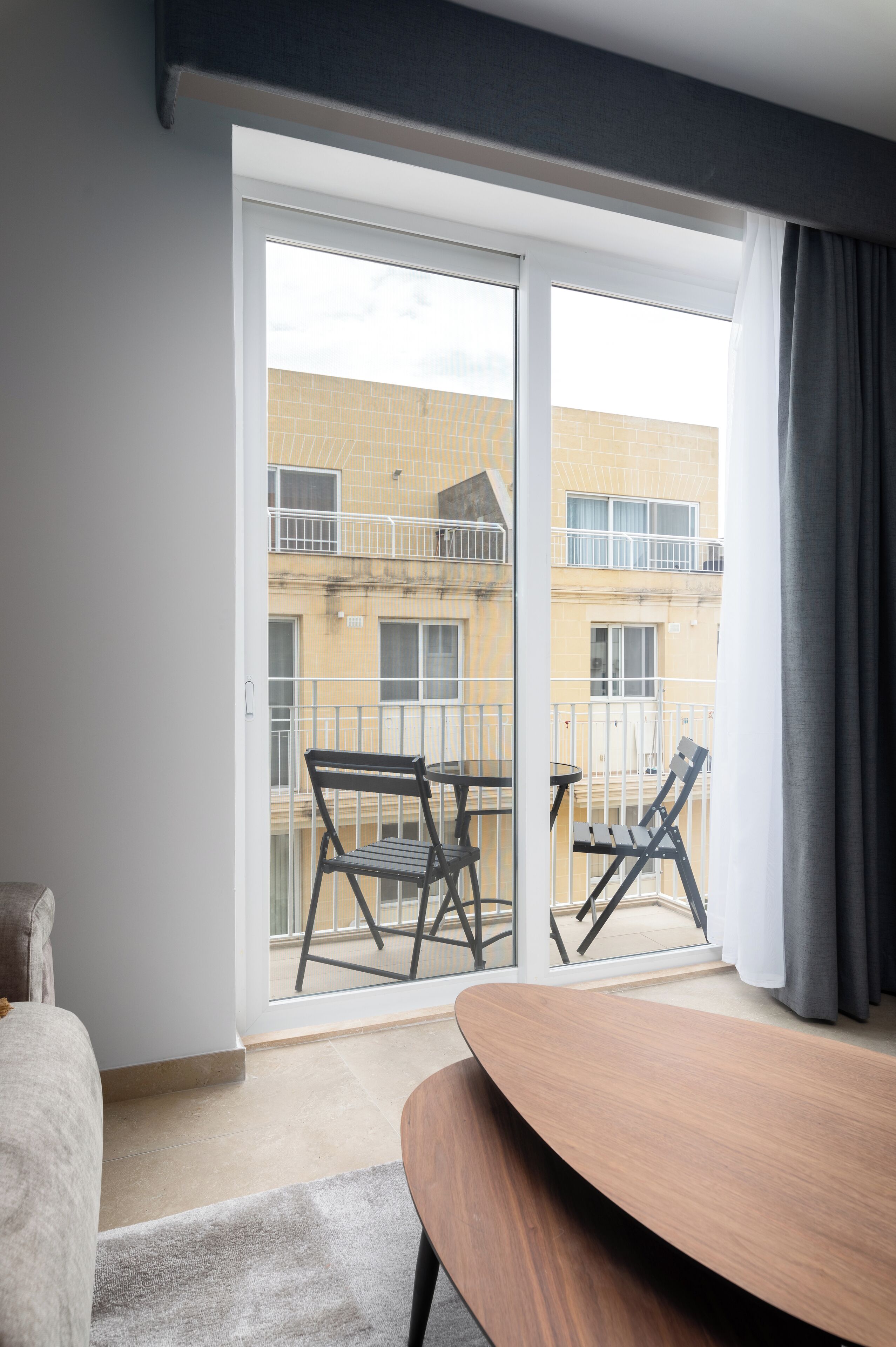 A room with a large sliding glass door leading to an outdoor balcony with two chairs and a table.
