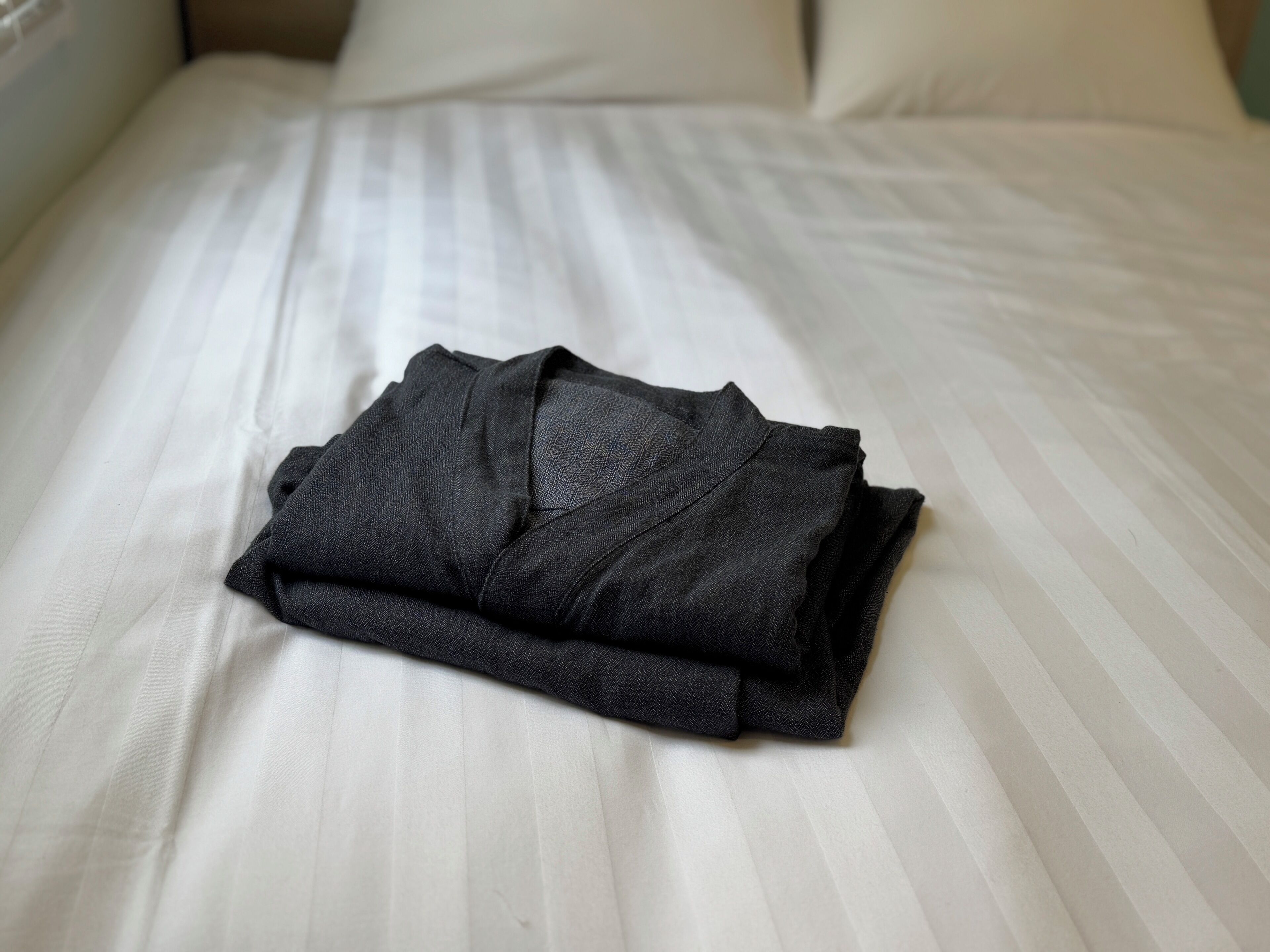 A neatly folded dark-colored garment on a bed with white bedding.