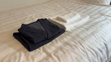 A neatly made bed with a folded black shirt and a folded white towel.