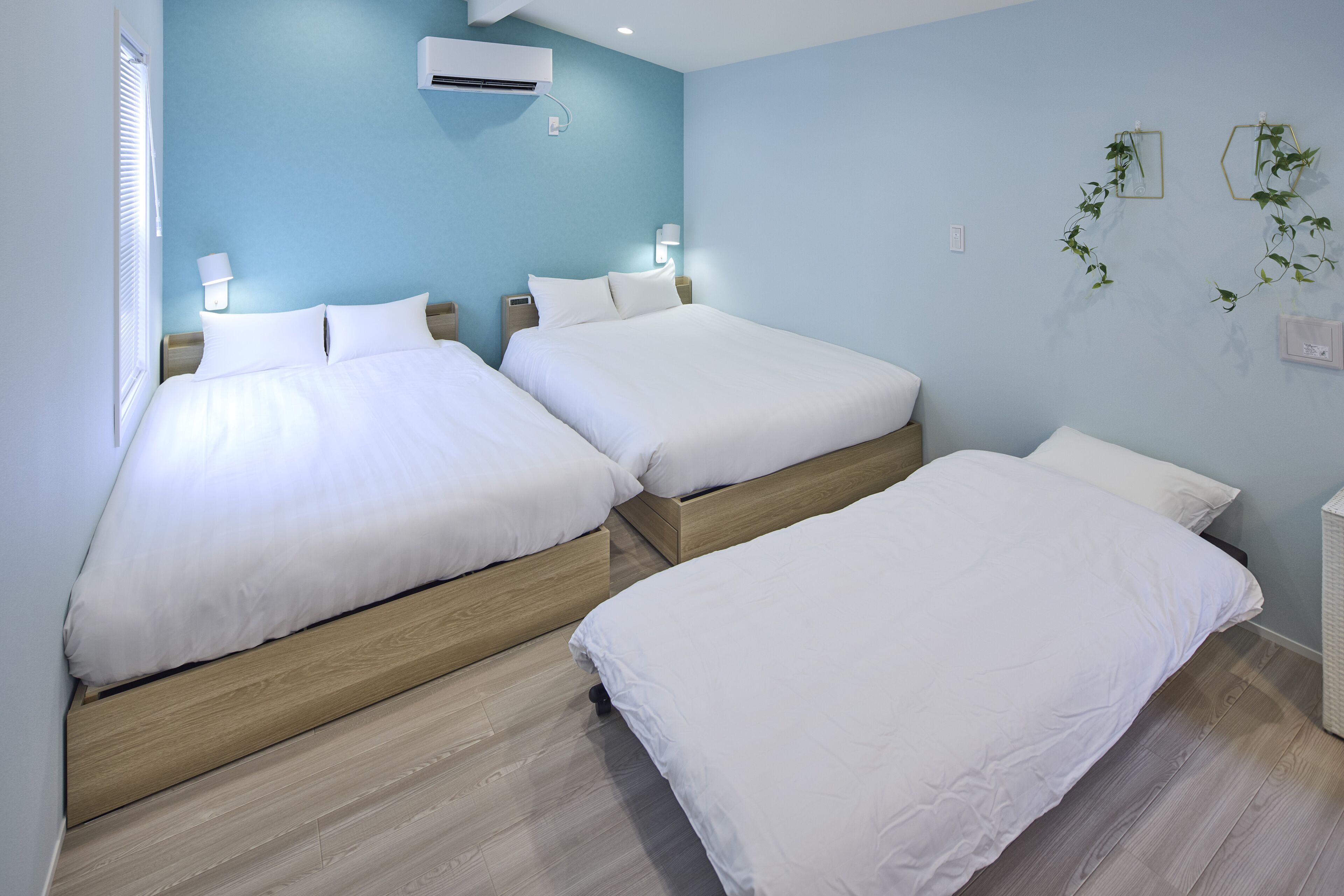 A hotel room with two beds, wooden headboards, a blue wall, and a wall-mounted air conditioner.
