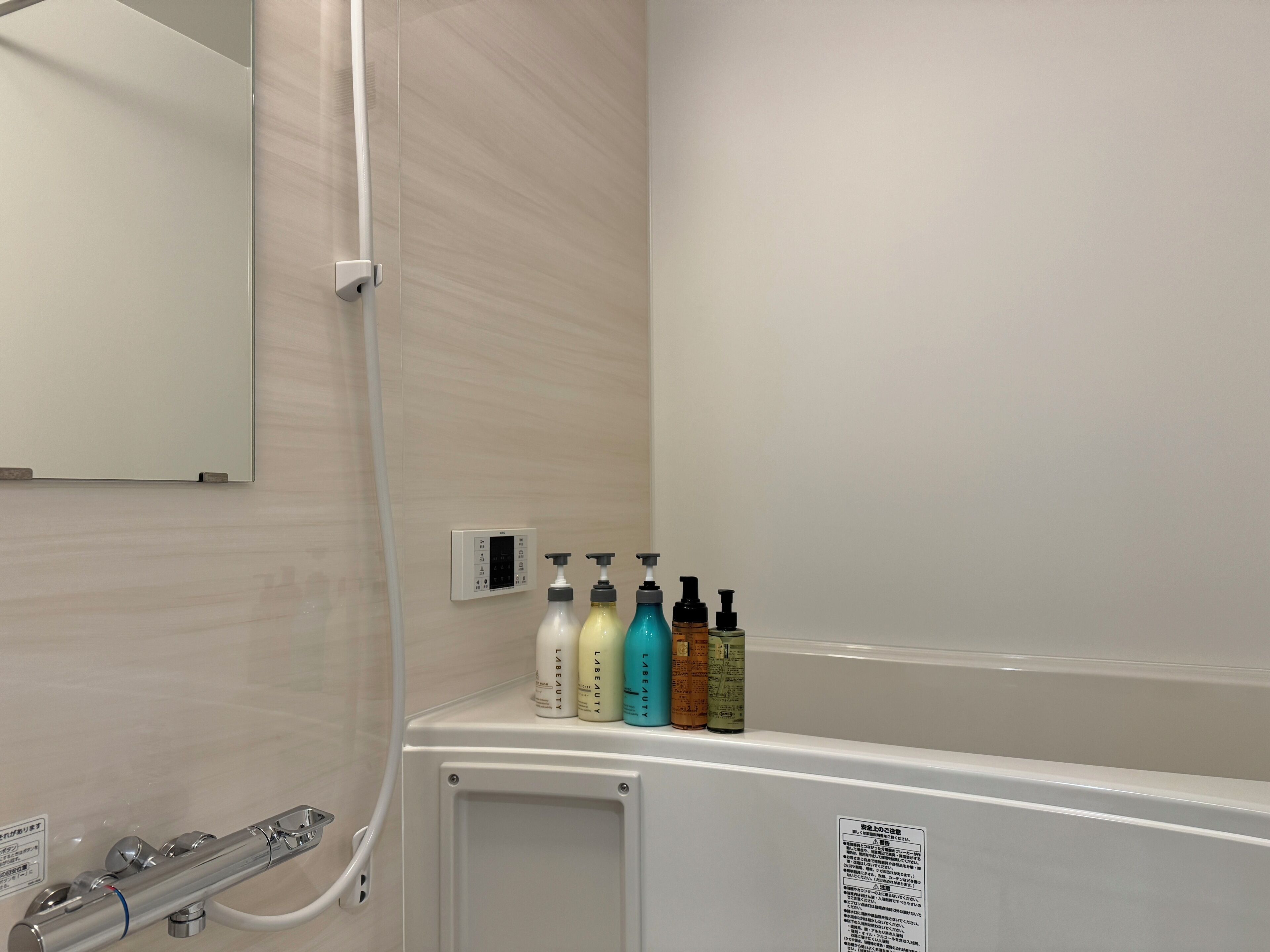Une salle de bain équipée d’une douche, d’un miroir et d’une étagère où sont rangés divers produits de toilette.