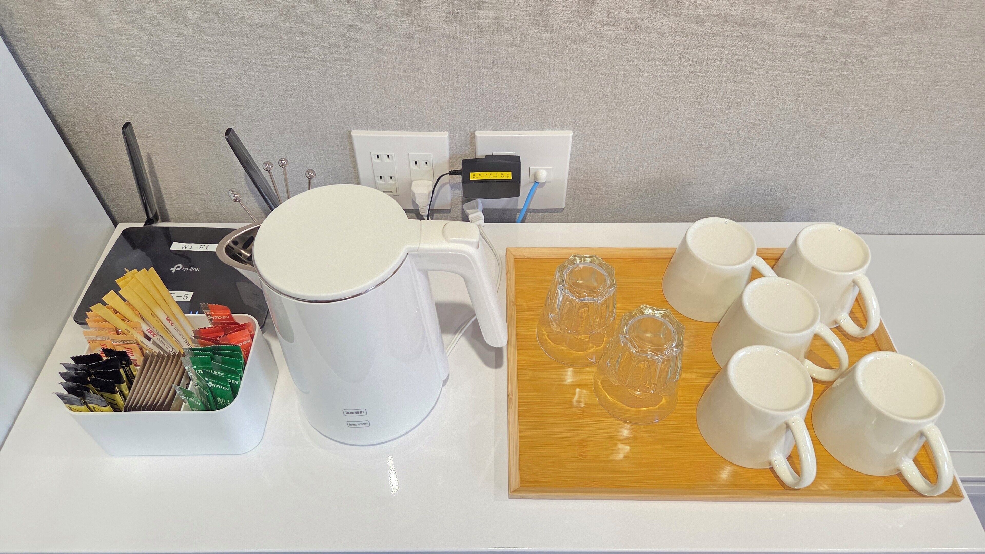 A coffee maker, a tray with mugs, and a box of tea packets on a table.