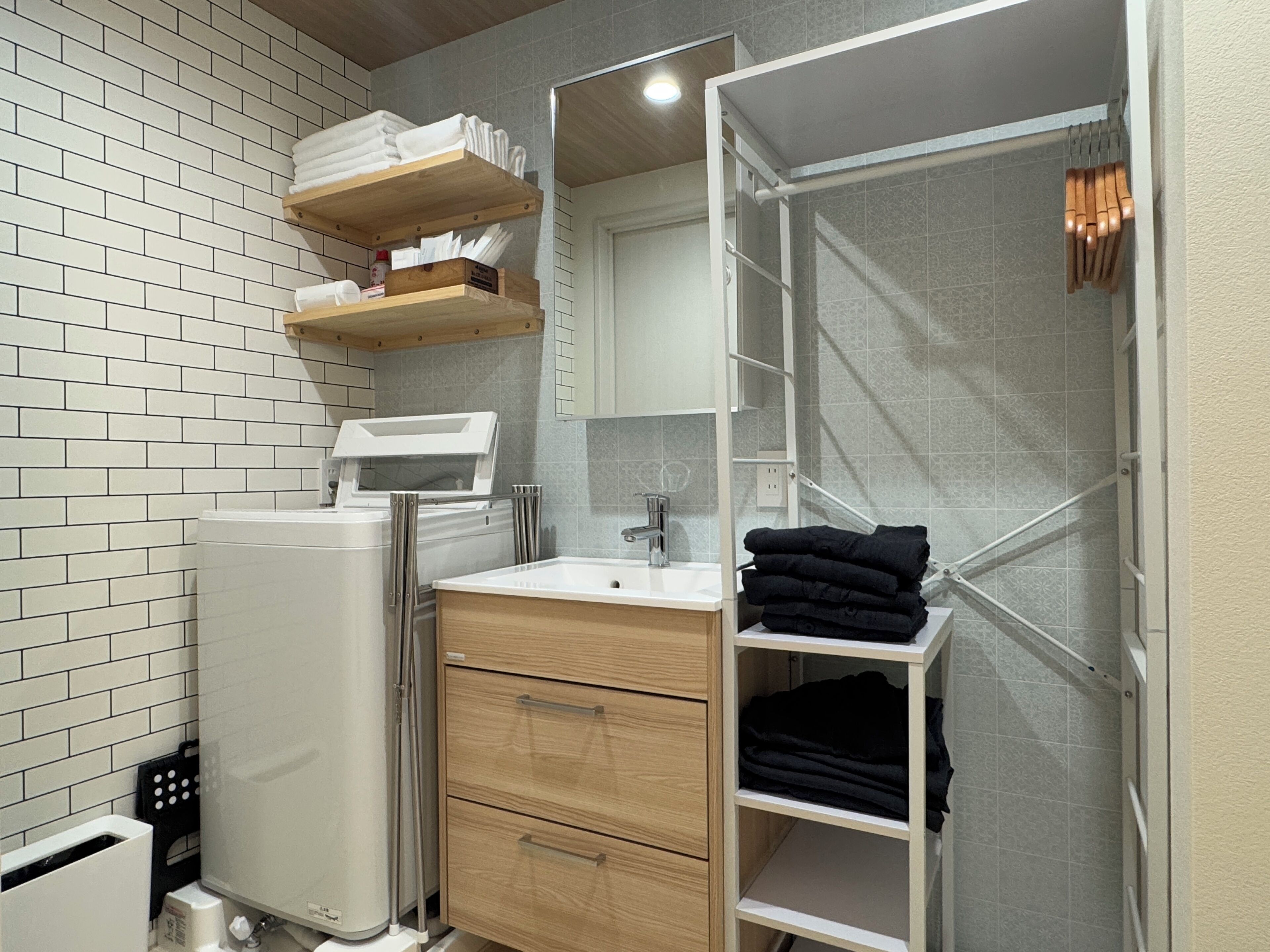 A bathroom with a white brick wall, a white sink, a wooden vanity, and a glass shower enclosure.
