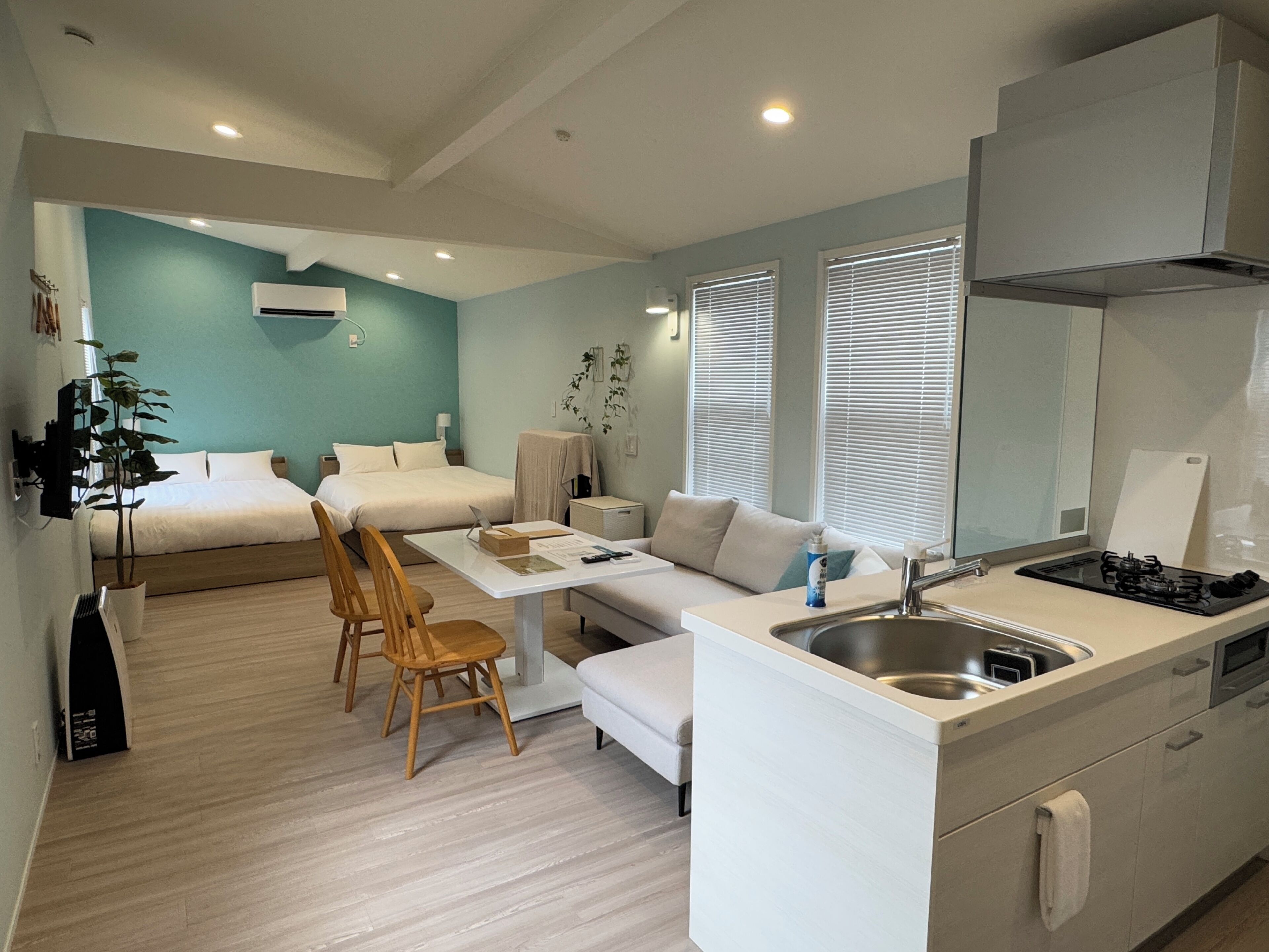 A modern hotel room with a kitchenette, a bed, a sofa, and a dining area.