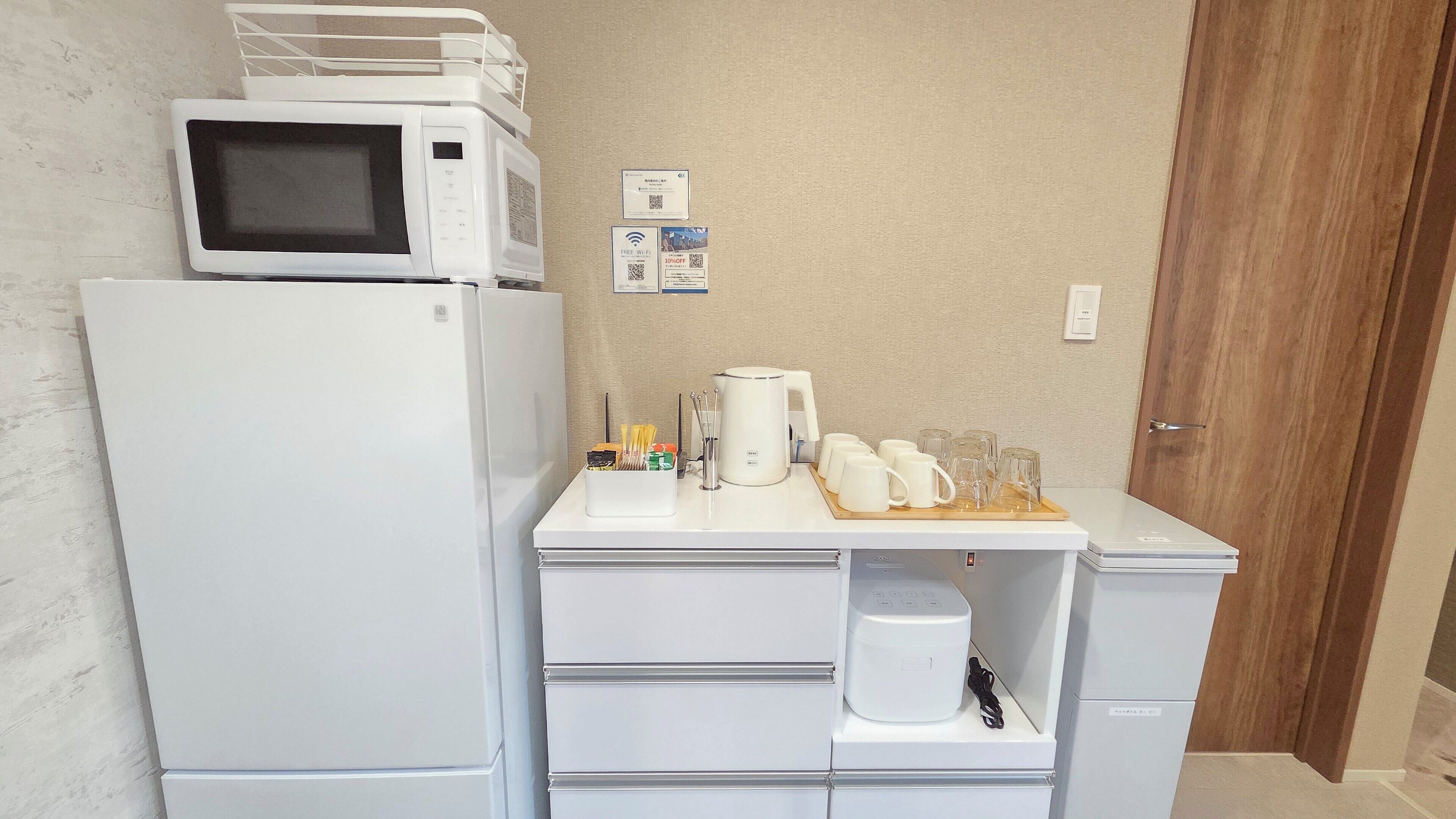 A compact kitchenette with a microwave, refrigerator, coffee maker, and a tray with cups and glasses.