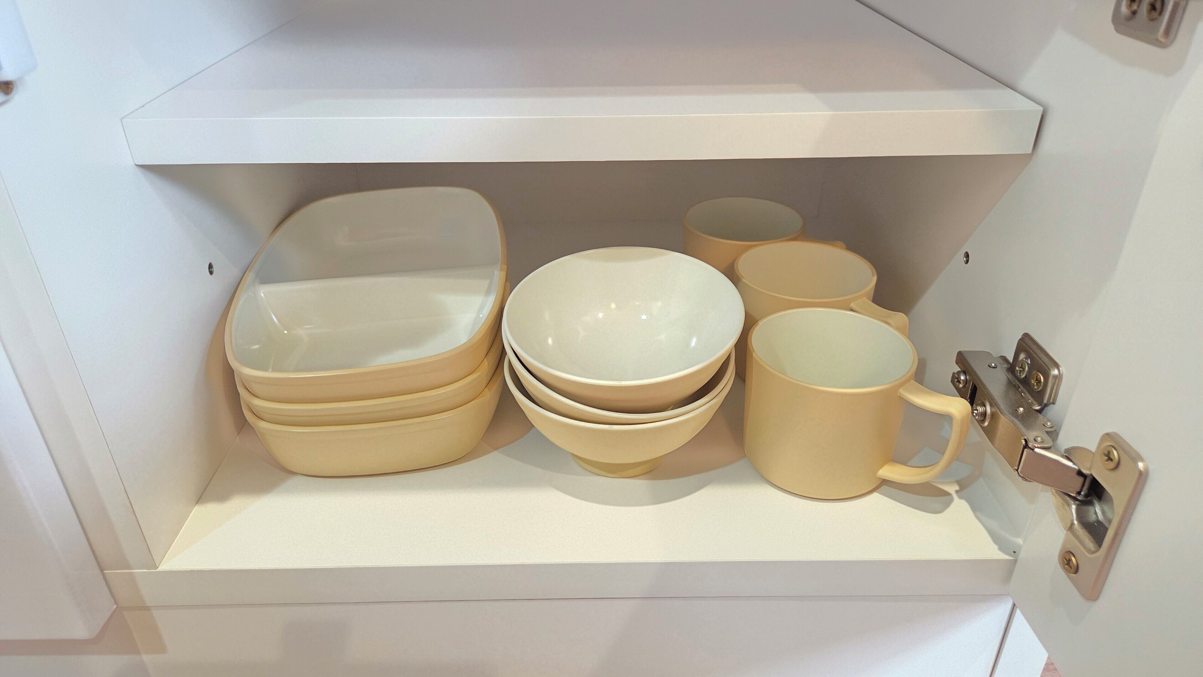 Un meuble de rangement contenant plusieurs bols et tasses de couleur beige.