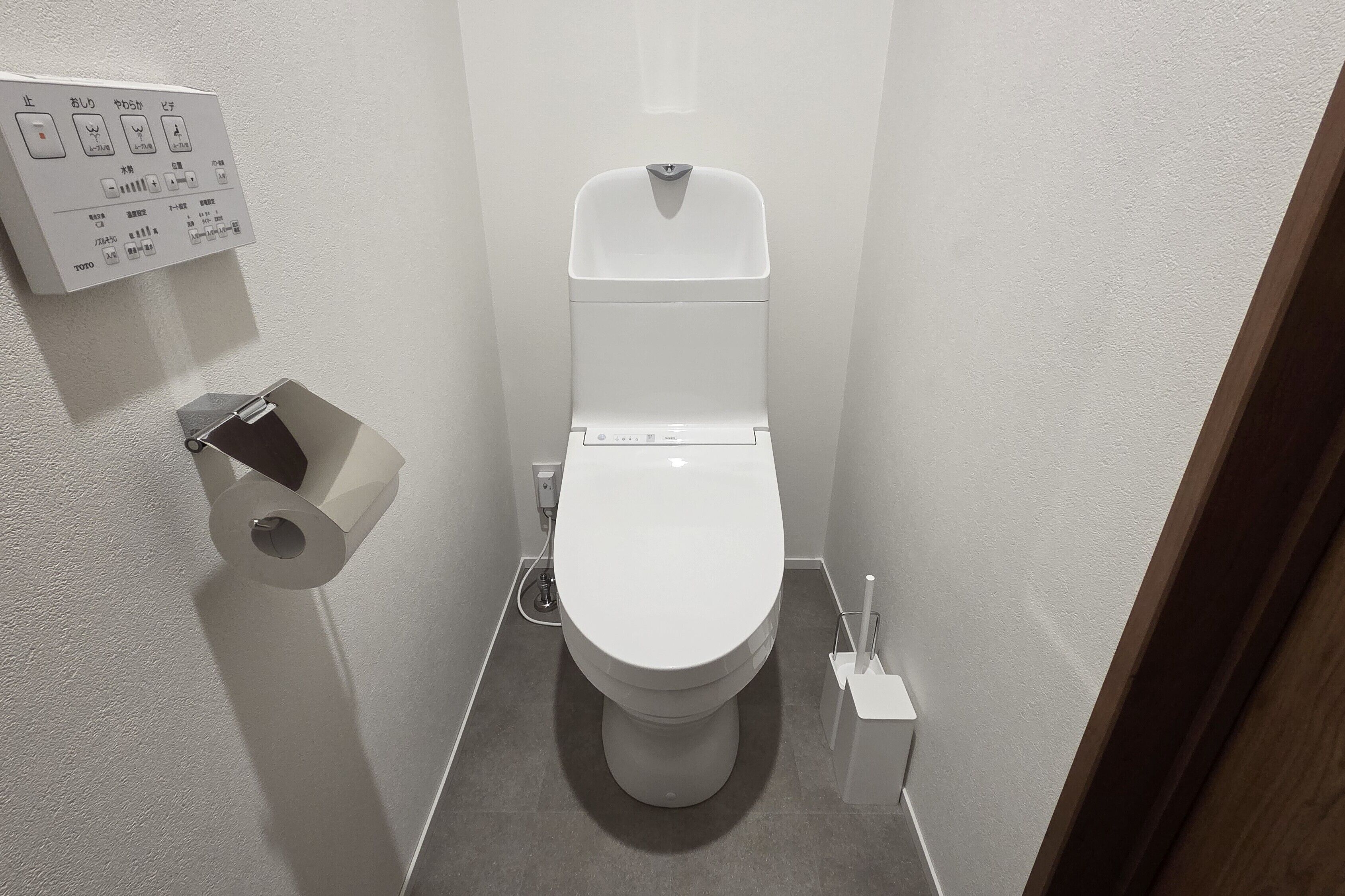 A small, modern bathroom with a toilet, a toilet paper holder, and a hand dryer.