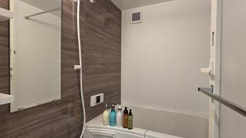 A modern bathroom with a shower, a mirror, and a shelf with toiletries.