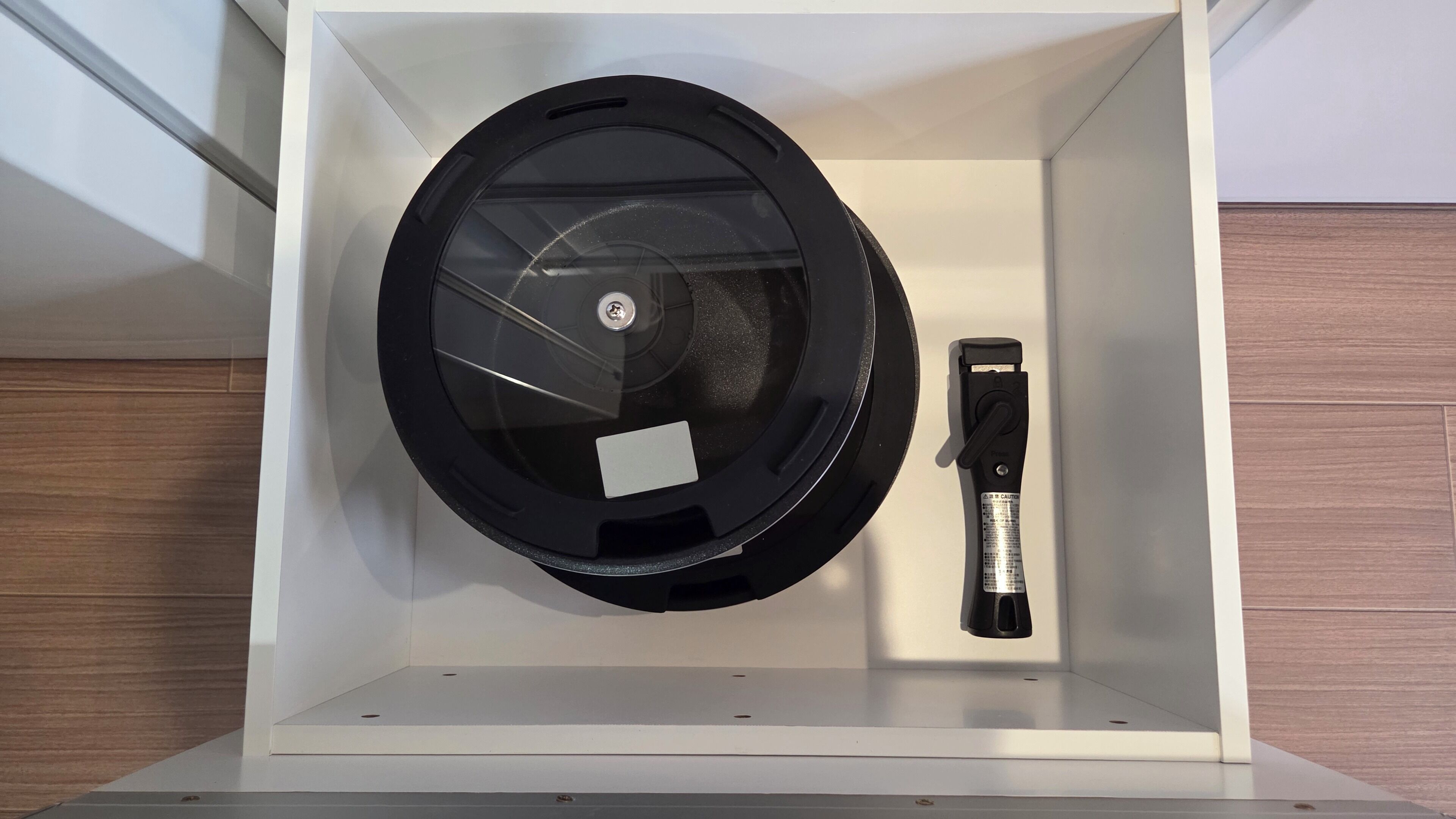 A compact, white storage box containing a black circular object with a handle, possibly a kitchen appliance or tool.