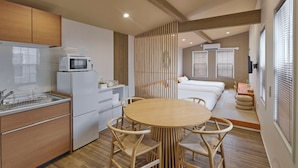 A modern kitchen with white appliances, a dining area with a round table and wooden chairs, and a bedroom with a bed and window blinds. - Solana Smart INN Fuji Gotenba  (Gotemba)
