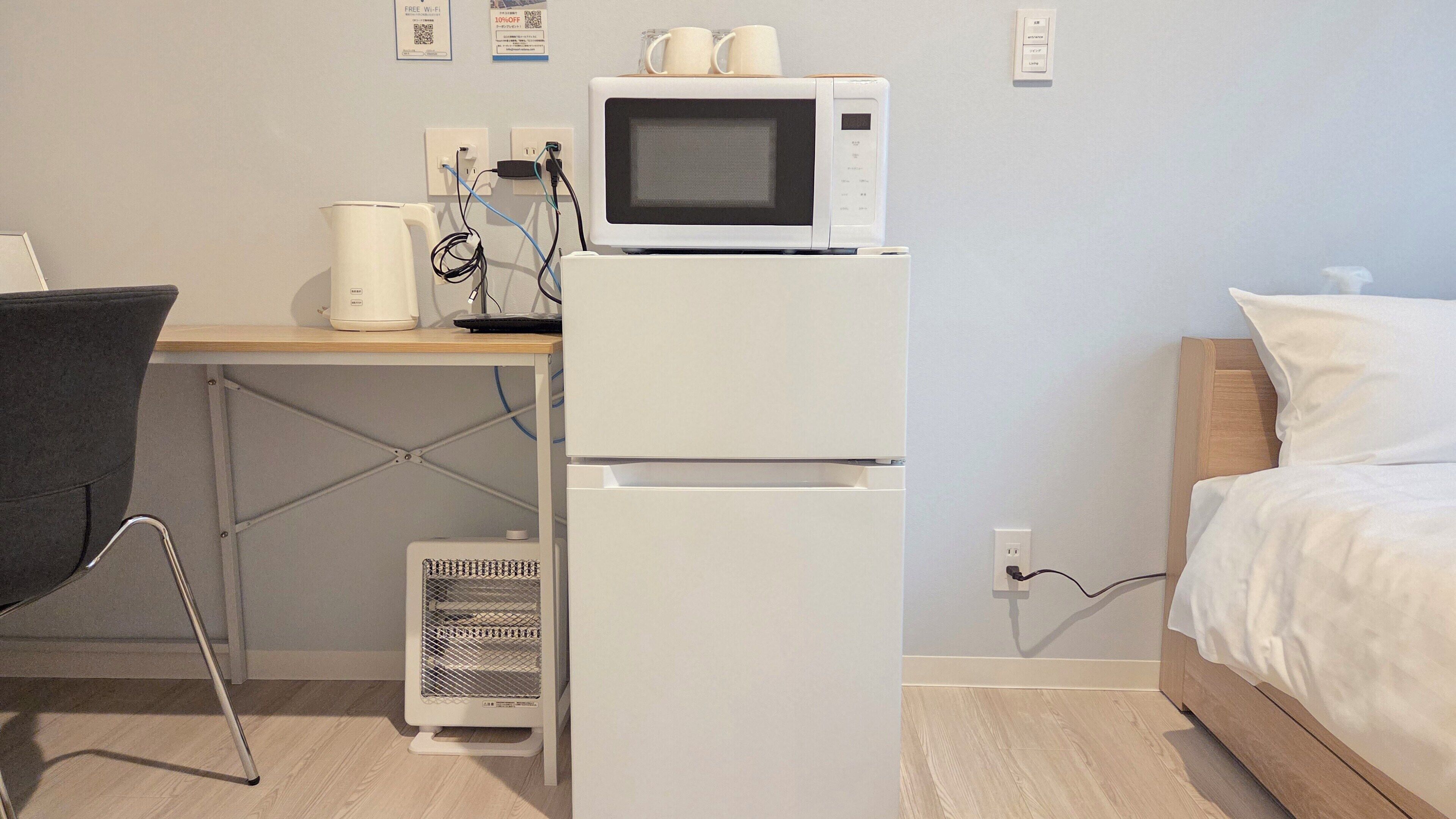 Une chambre d’hôtel compacte dotée d’une kitchenette, comprenant un four à micro-ondes, une bouilloire et une machine à café. Elle comprend également un bureau avec une chaise, un lit et un radiateur.