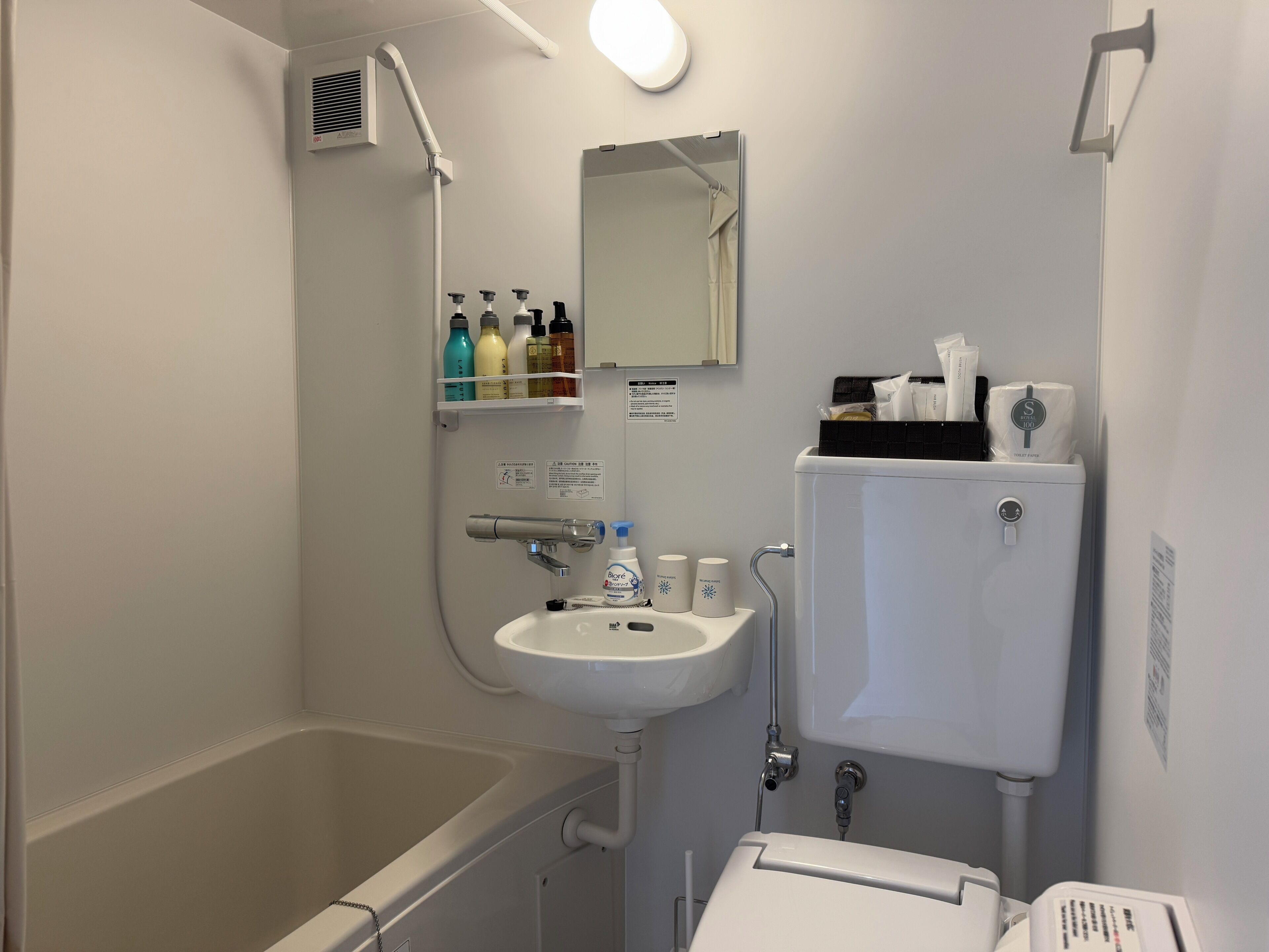 A bathroom with a bathtub, a sink, a mirror, and a toilet. There are toiletries on the sink and a showerhead above the bathtub.