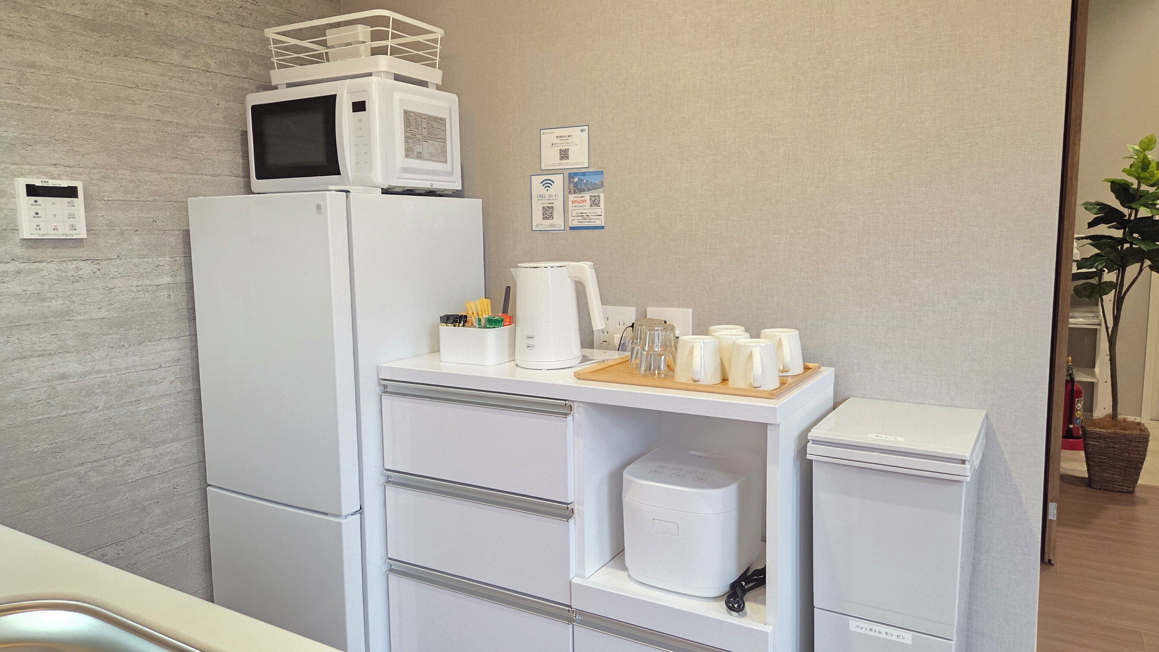 A compact kitchenette with a microwave, refrigerator, and a small countertop with a kettle, cups, and utensils.