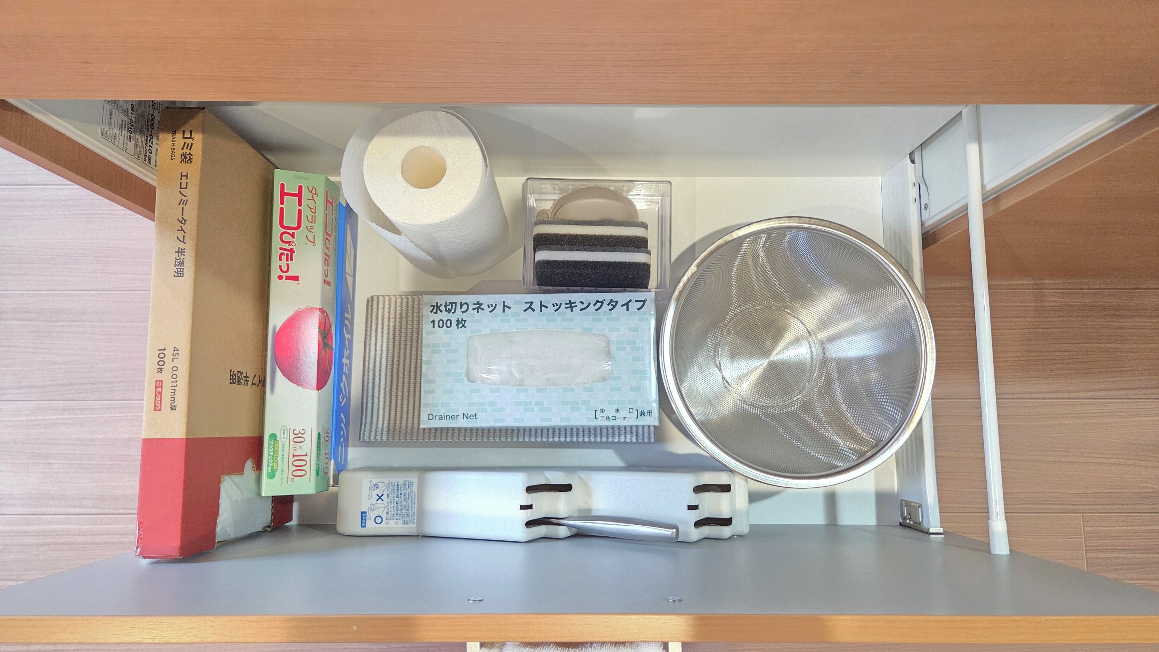 A kitchen shelf with a roll of toilet paper, a box of paper towels, a metal strainer, and a white plastic container.