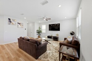 A modern living room with a brown sofa, a glass coffee table, and a ceiling fan. - 4BR North Jax Peaceful Retreat, 8 minutes from Jax airport (Jacksonville)