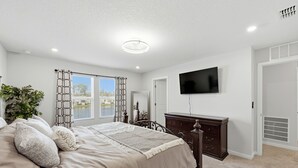 Ein Schlafzimmer mit Bett, Kommode, Fernseher und einem Fenster mit Vorhängen.