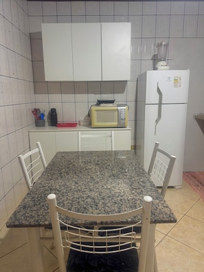 Cozinha com armários brancos, micro-ondas, geladeira e bancada de granito.