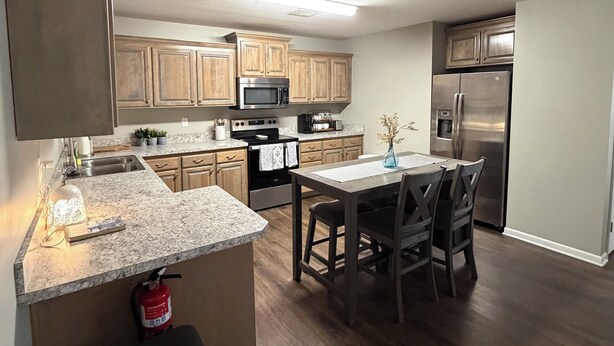 A modern kitchen with wooden cabinets, stainless steel appliances, a granite countertop, and a dining area with a table and chairs. - Tremendous 3-bedroom townhome with close to Cave Hollow Park in Warrensburg (Warrensburg)