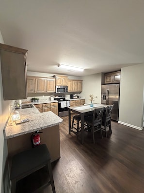 A modern kitchen with wooden cabinets, stainless steel appliances, a granite countertop, and a dining area with a table and chairs.