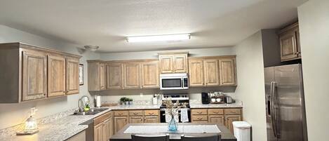A modern kitchen with wooden cabinets, a stainless steel refrigerator, and a central island with seating.
