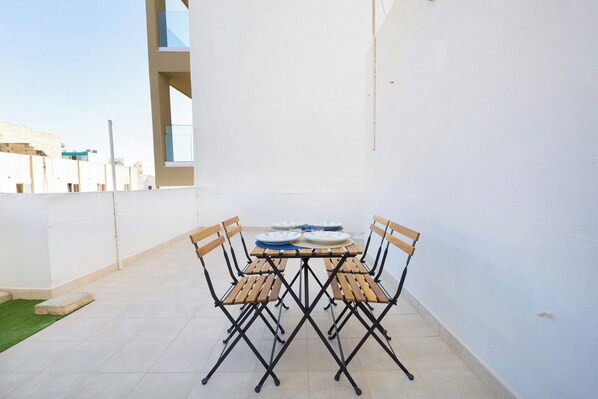A patio with a table and chairs, a tiled floor, and a white wall. - 2BR Penthouse with Large Front Terrace (St. Paul's Bay)