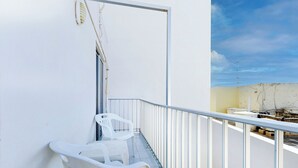 Un balcón con sillas de plástico blanco, baranda de metal y vista al cielo y un edificio al fondo.