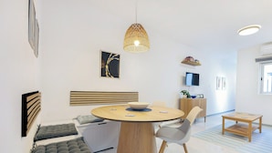 Una sala de estar moderna con una mesa redonda de madera, un sofá con cojines, un televisor y una lámpara colgante decorativa.