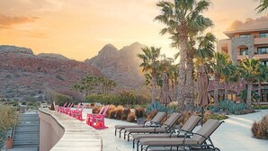 Ein Poolbereich eines Resorts mit Liegestühlen und Sonnenschirmen, umgeben von Palmen und Wüstenlandschaft.