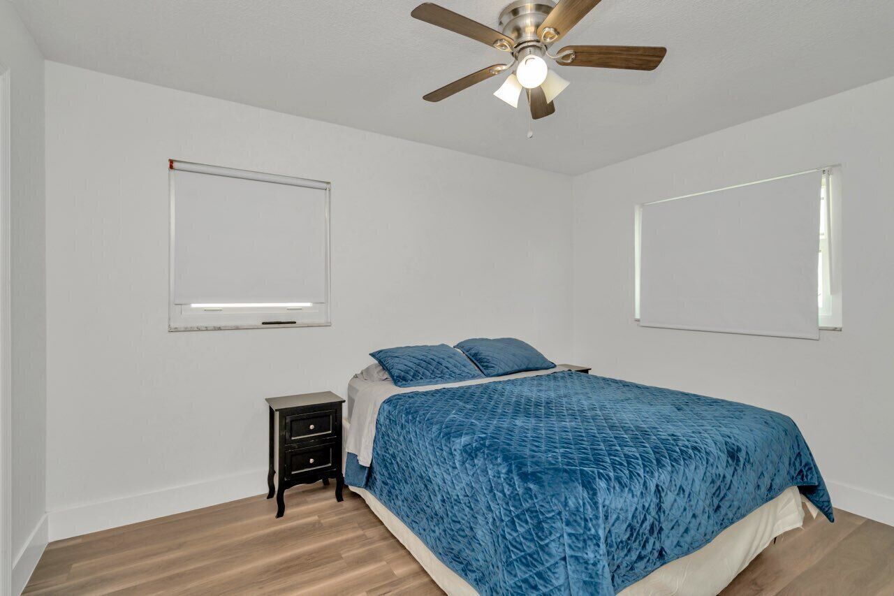A bedroom with a bed, a nightstand, a ceiling fan, and two wall-mounted light fixtures.