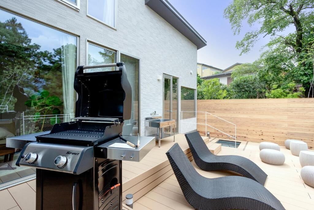 Una cocina exterior moderna con una parrilla, un comedor con mesa y sillas, y una terraza de madera.