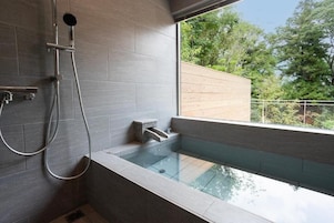 Un baño moderno con una bañera de hidromasaje con cerramiento de vidrio, zona de ducha y vistas al exterior.