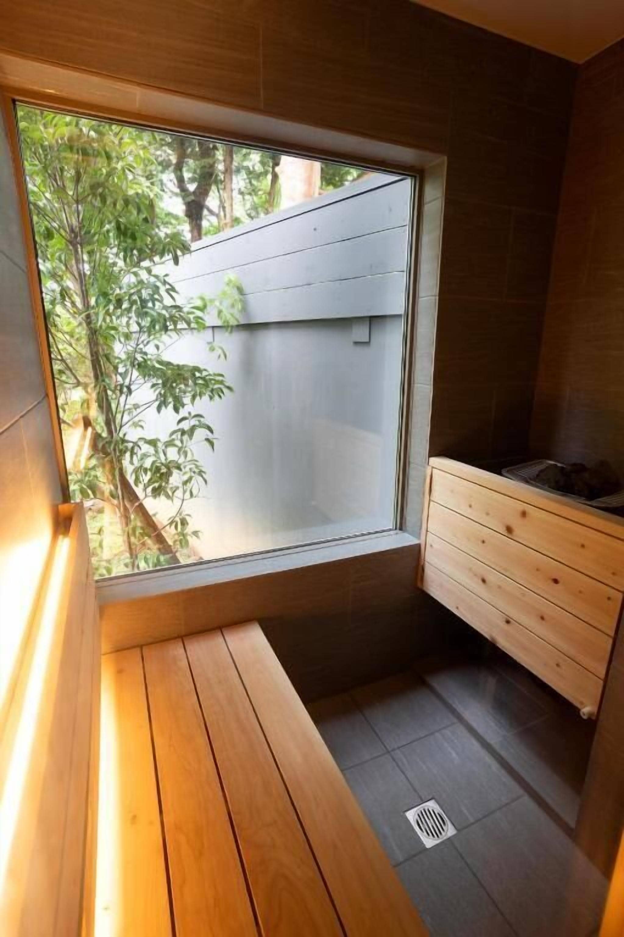 A small bathroom with a wooden bench, a wooden cabinet, and a window with a view of greenery outside.