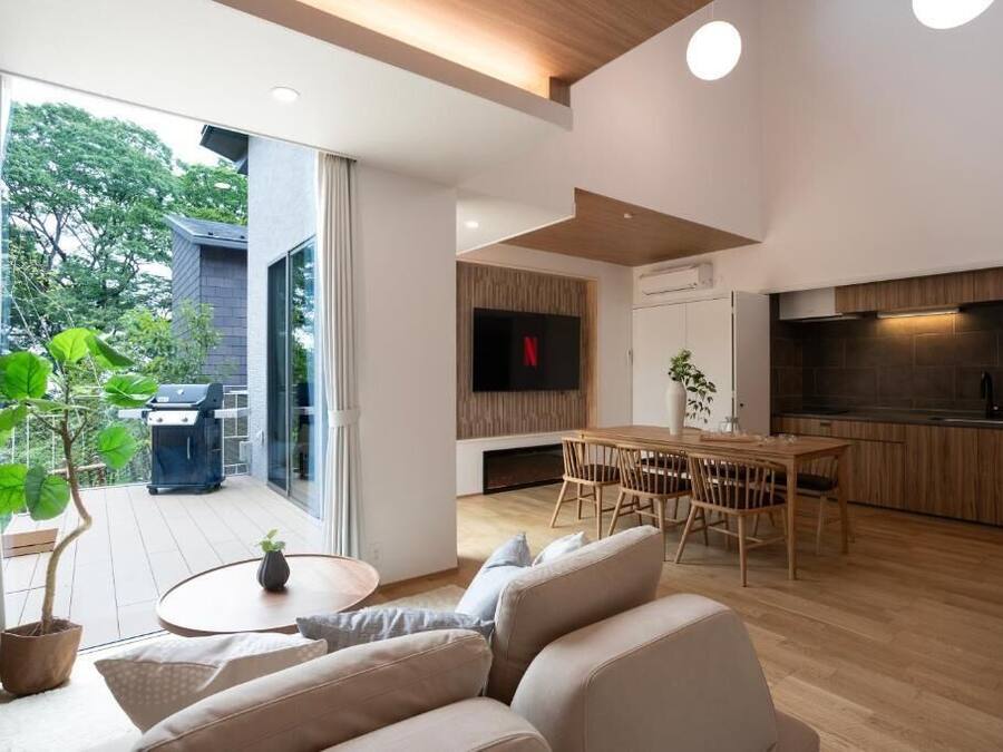 A modern living room with a sofa, dining table, and TV. There is a kitchen area with a stove and cabinets.