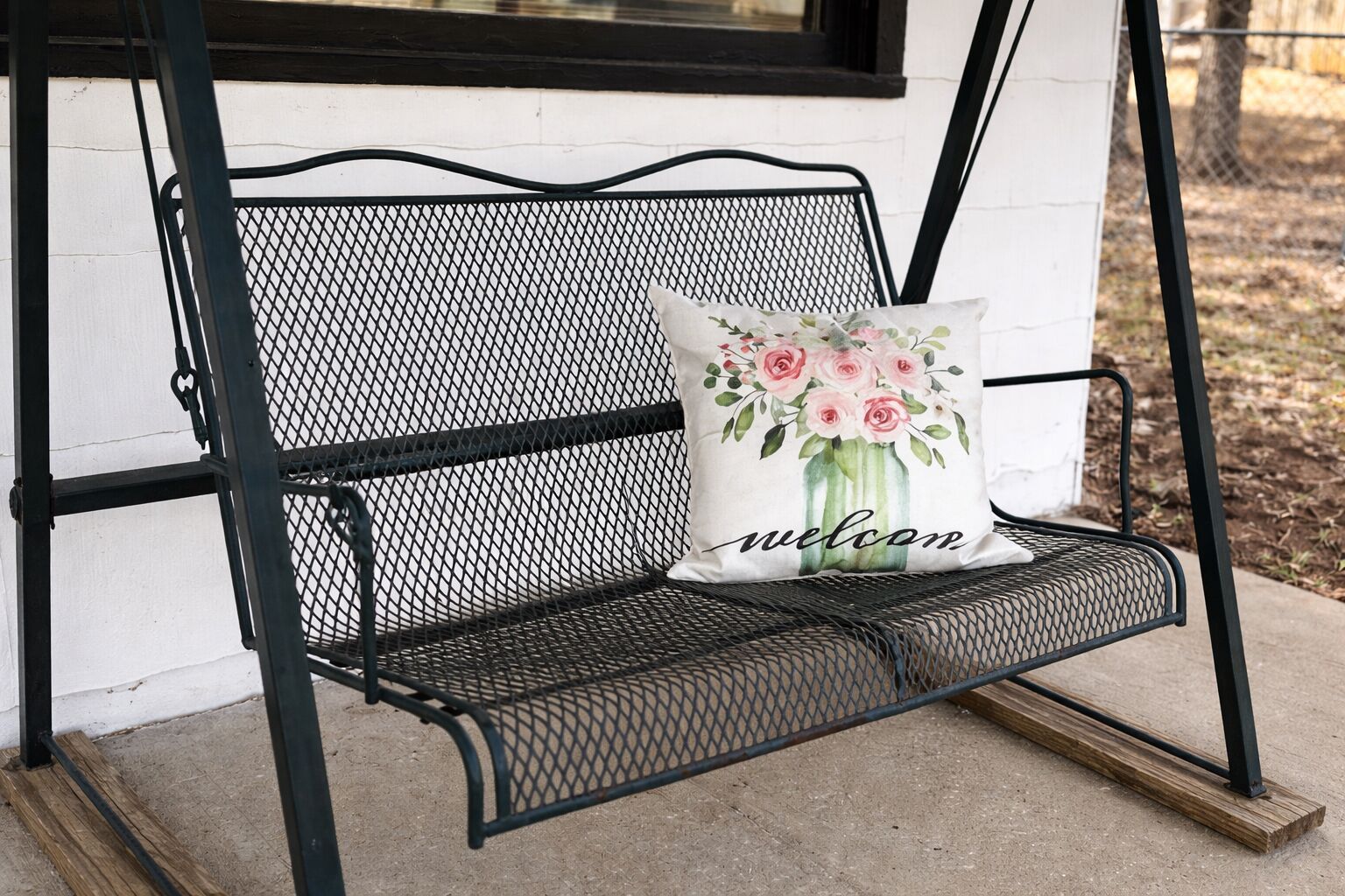 A black metal bench with a white cushion featuring a floral design and the word "welcome".
