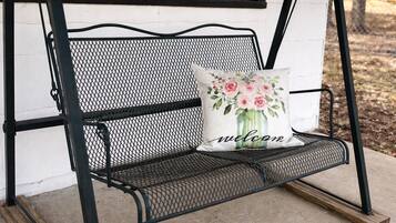 A black metal bench with a white cushion featuring a floral design and the word "welcome".