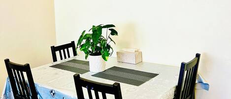 A dining area with a table set for four, a potted plant, and a painting of a tree on the wall.