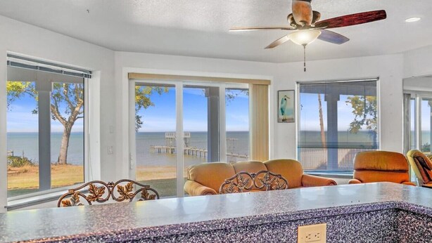 A room with a view of the sea, a ceiling fan, and a seating area with a table. - Salty Bay Hideaway (Gulf Breeze)